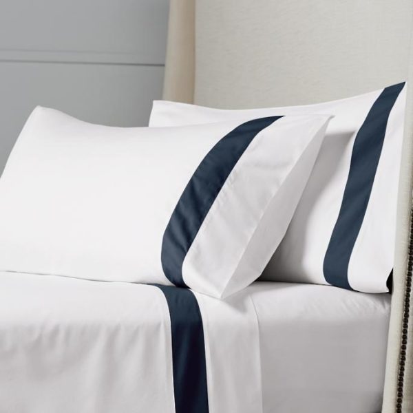 Ensemble de lit Navy intemporel et polyvalent en satin de coton blanc avec une bande contrasté en bleu marine rappelant le style marin .